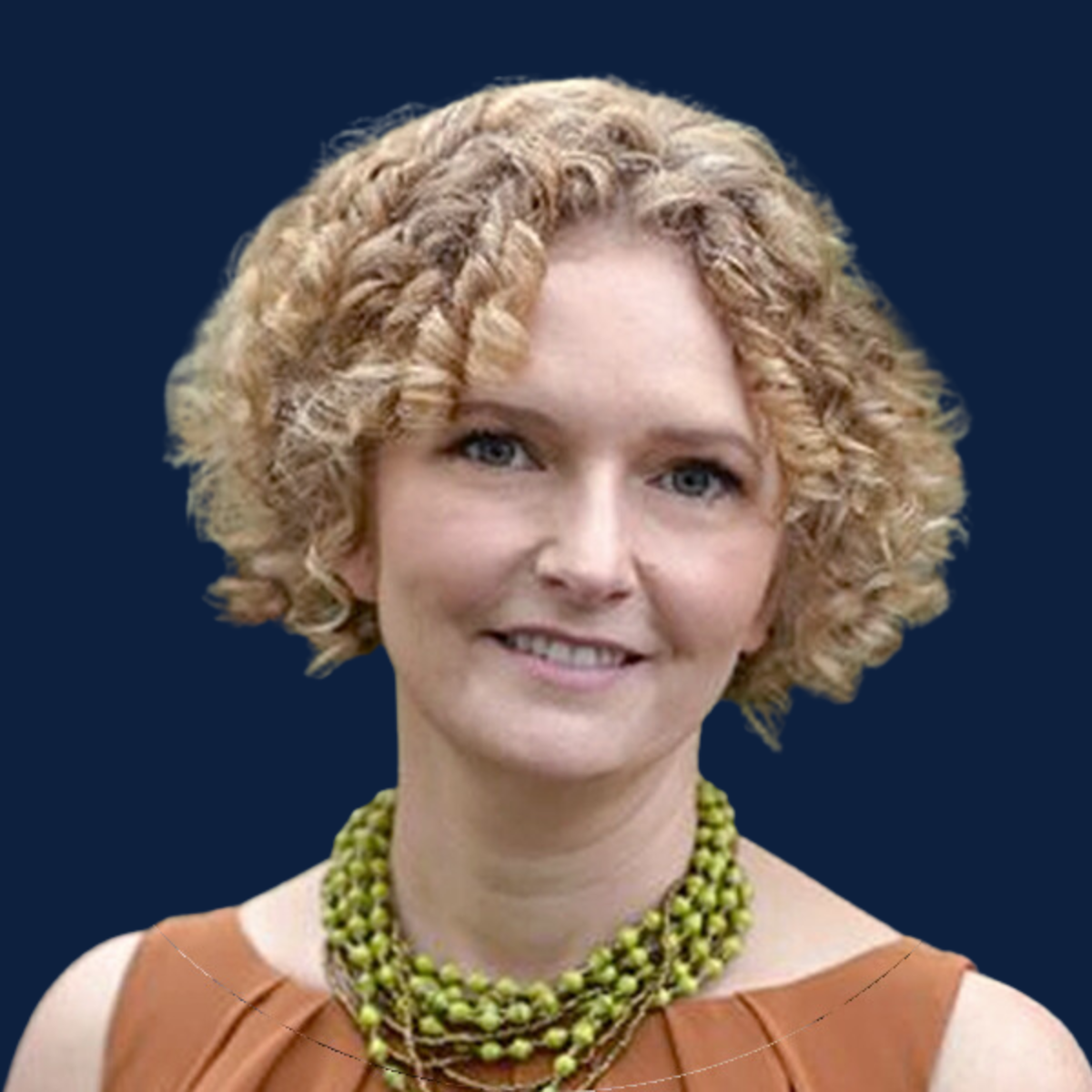 Greatest Good Member Feature, Nimmity from All of the Good Things A headshot of a smiling woman with curly blonde hair wearing a green beaded necklace and an orange sleeveless top. The background is a solid dark blue.